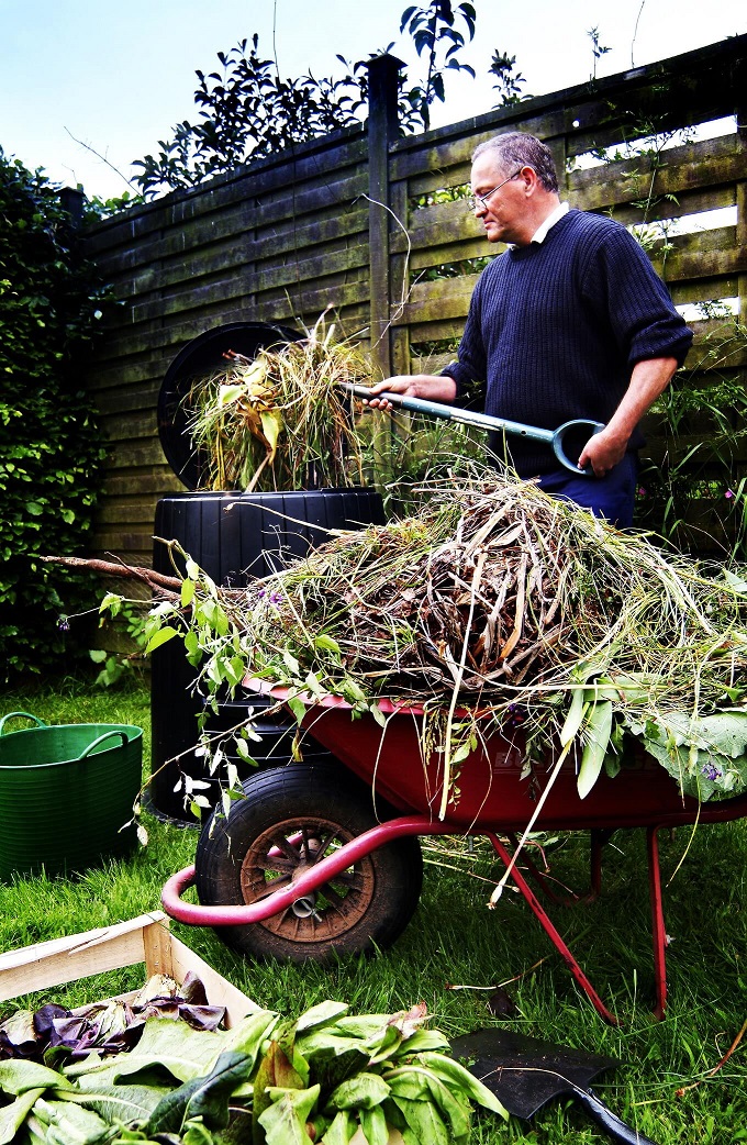 man composting in garden with wheelbarrow