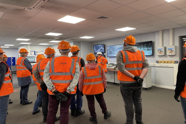 A group of people wearing orange safety vests and hard hats at a site visit